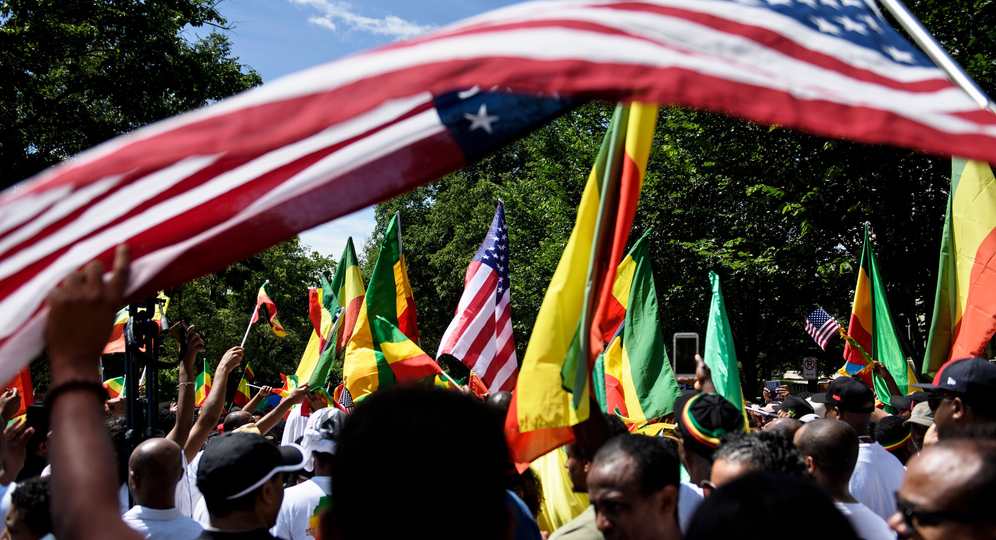 Group of primarily Black individuals hold flags, including Ethiopian and U.S. flags