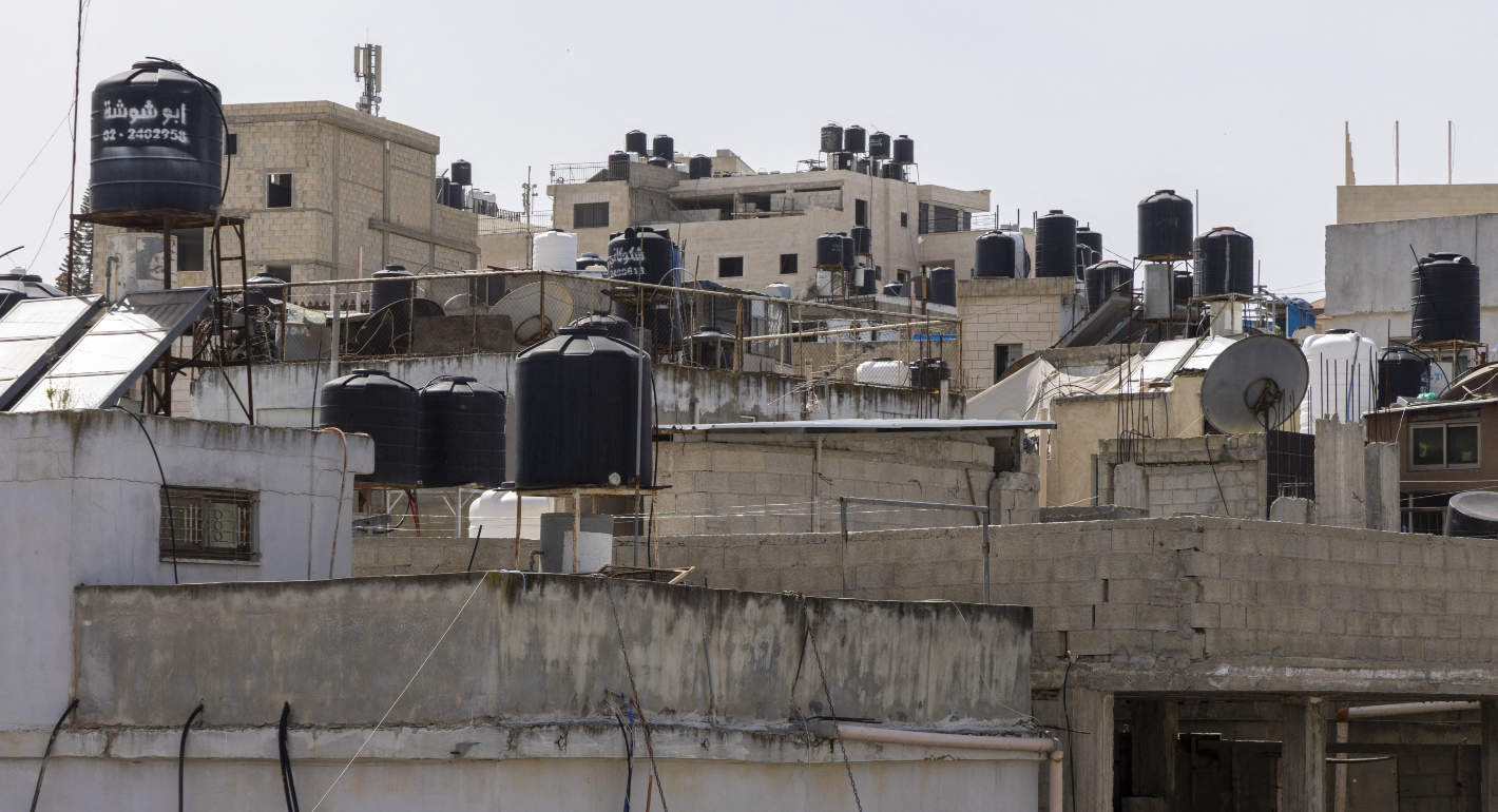 Buildings in Ramallah with black water jugs on top.