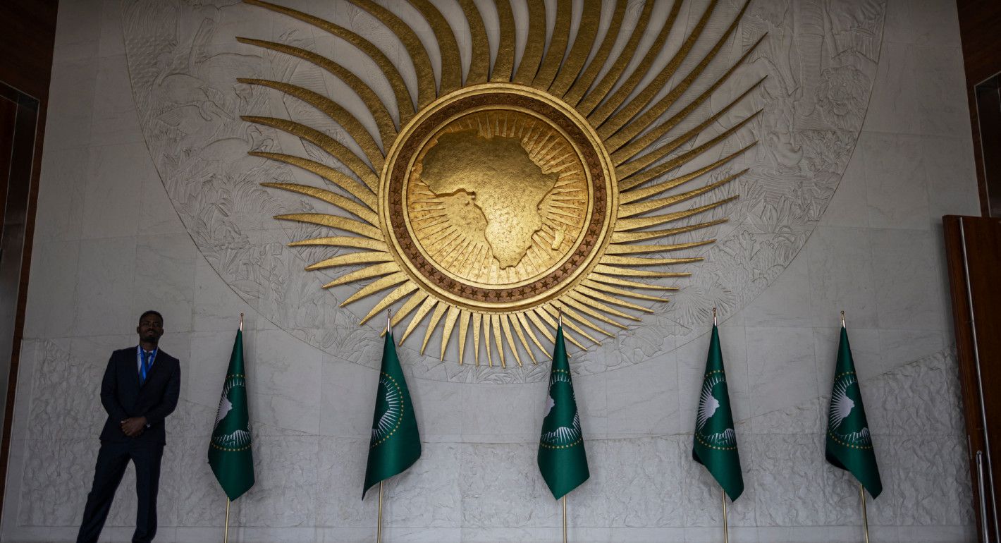 Photograph of a security guard standing in front of the African Union logo in the union's main plenary hall.