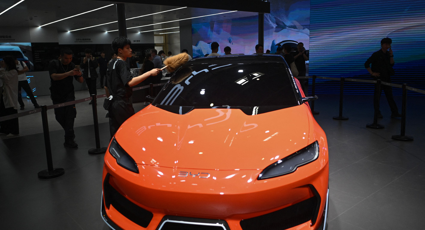 A man dusting an orange BYD electric car at an auto show