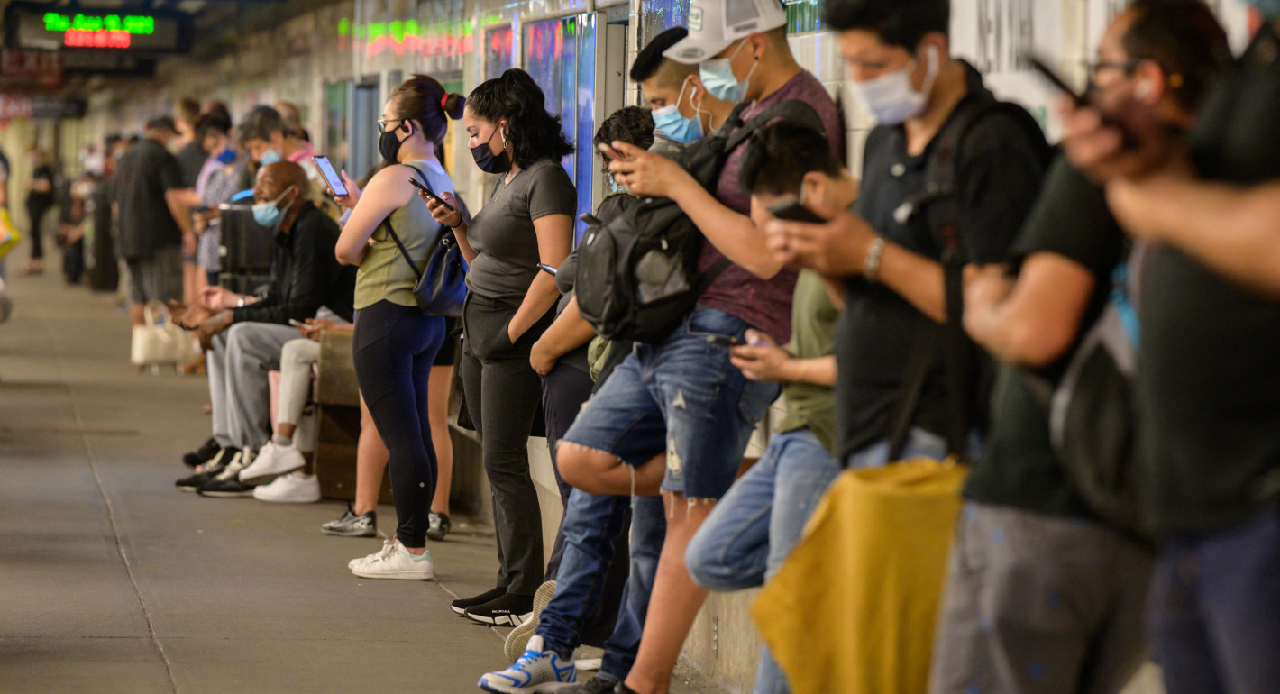 People look at their phones while waiting for a train