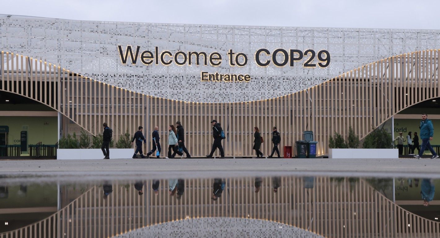 People walking outside a building with a Welcome to COP29 Entrance sign