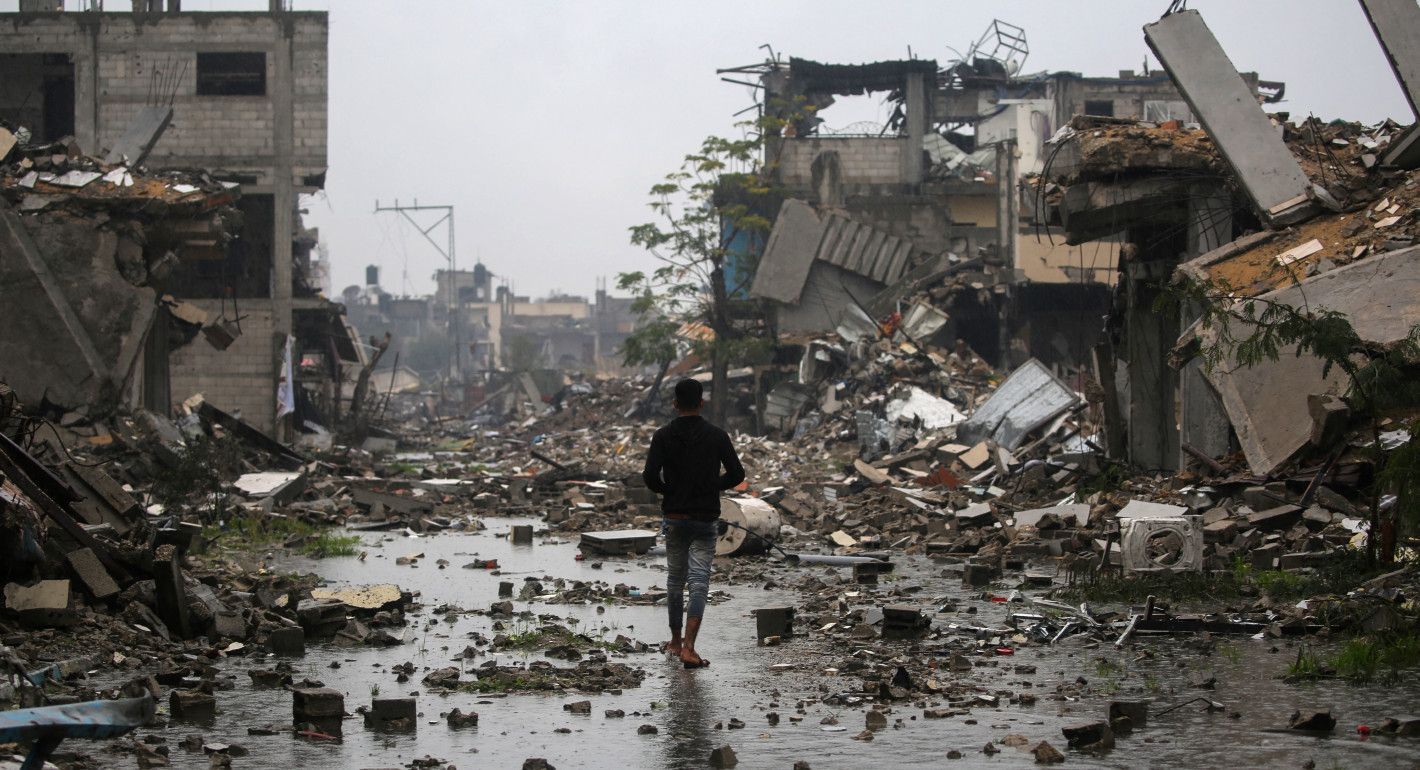 A teenage boy walks in the rain amid the remains of destroyed buildings