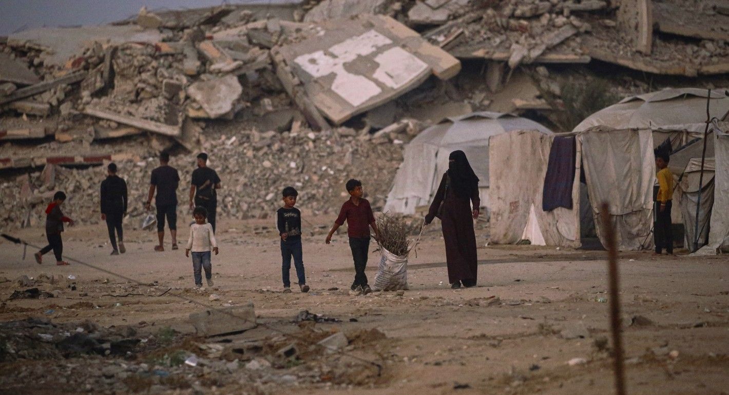 A woman a children dragging a bag of wood amid rubble