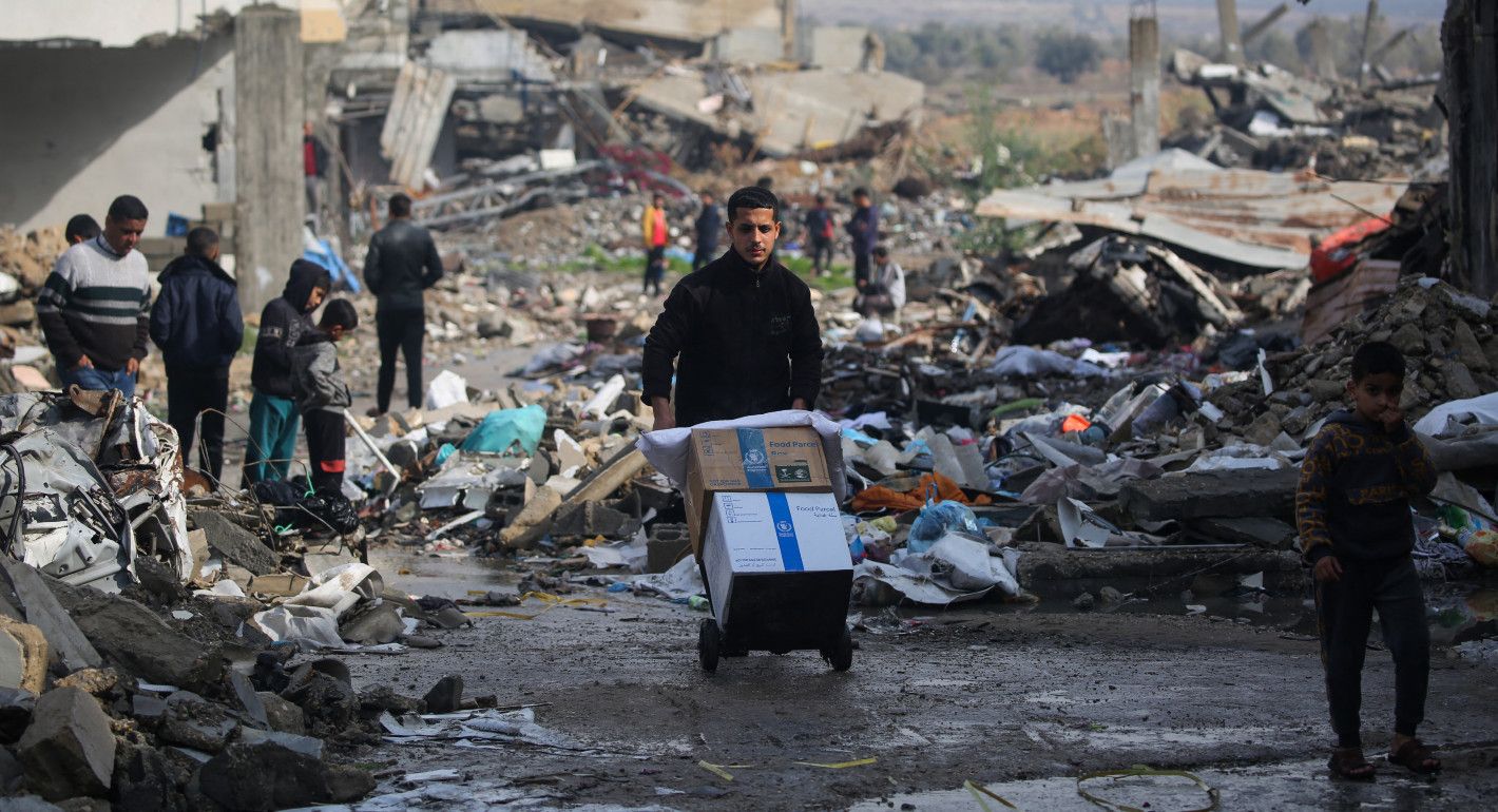 Boy hauling boxes of food on a dolly amid destroyed buildings