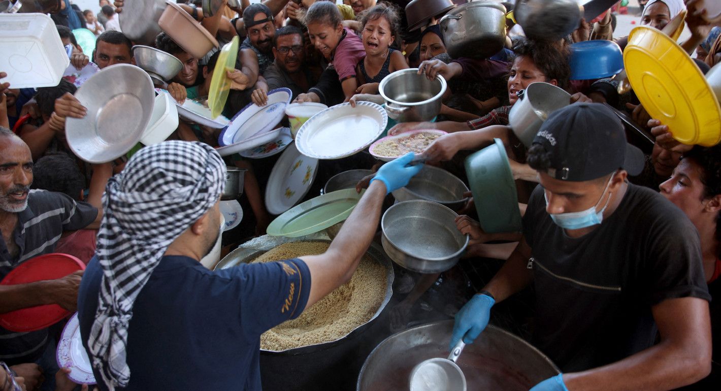 men serve food out of bit soup vats to a crowd pushing their bowls forward at them