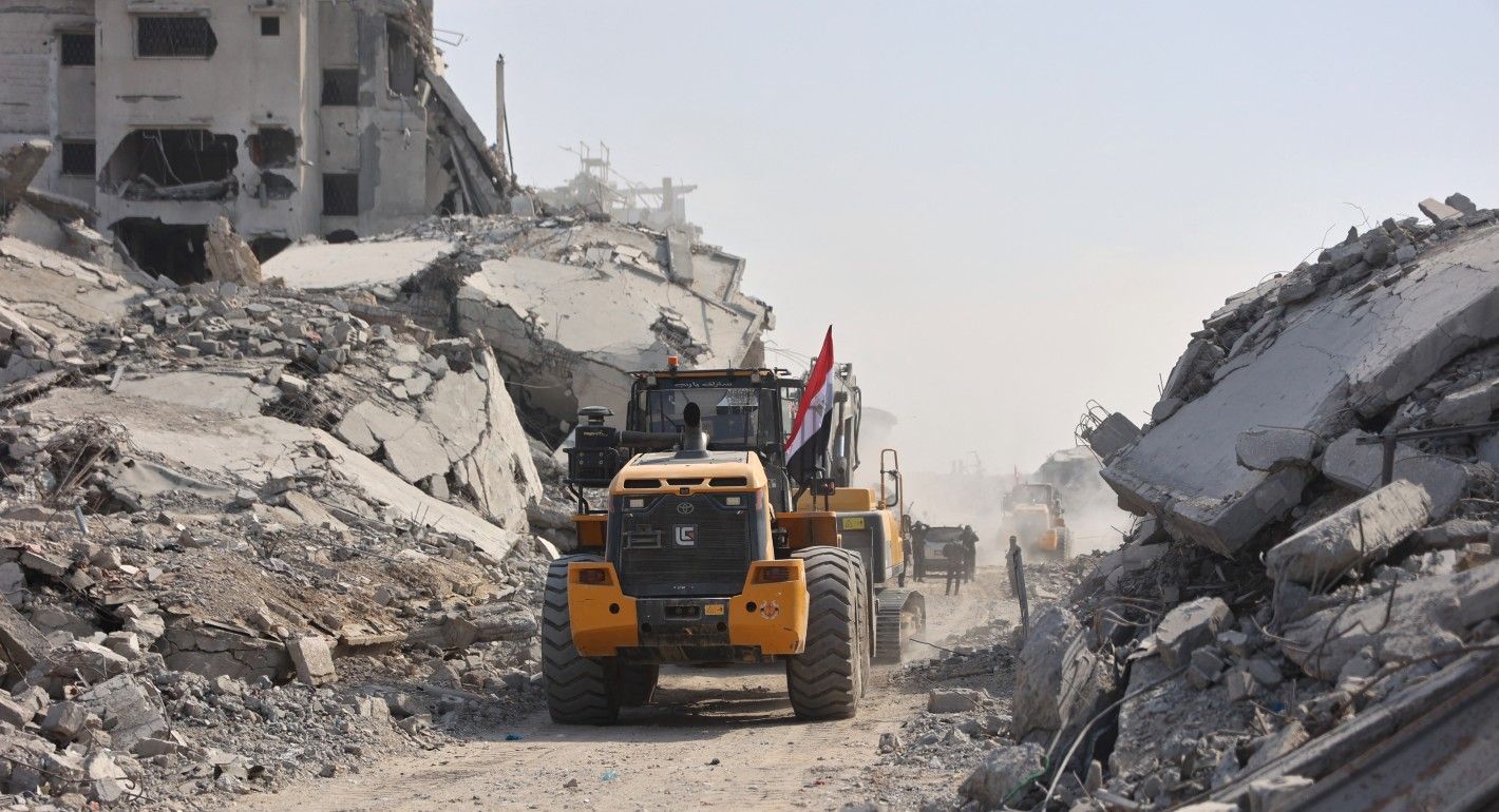 Bulldozer driving by destroyed buildings