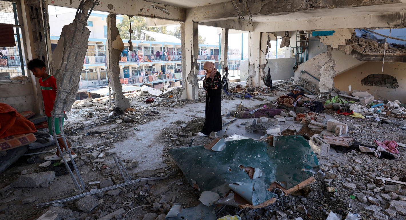 A woman stands amid rubble in a bombed-out room that used to be a school classroom.