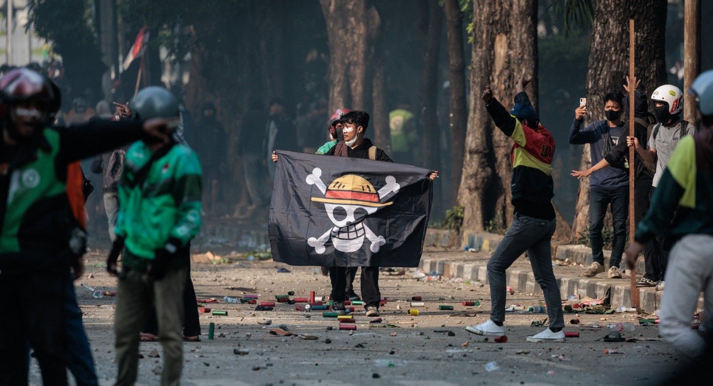 Man holding a One Piece flag standing in a street with other protesters