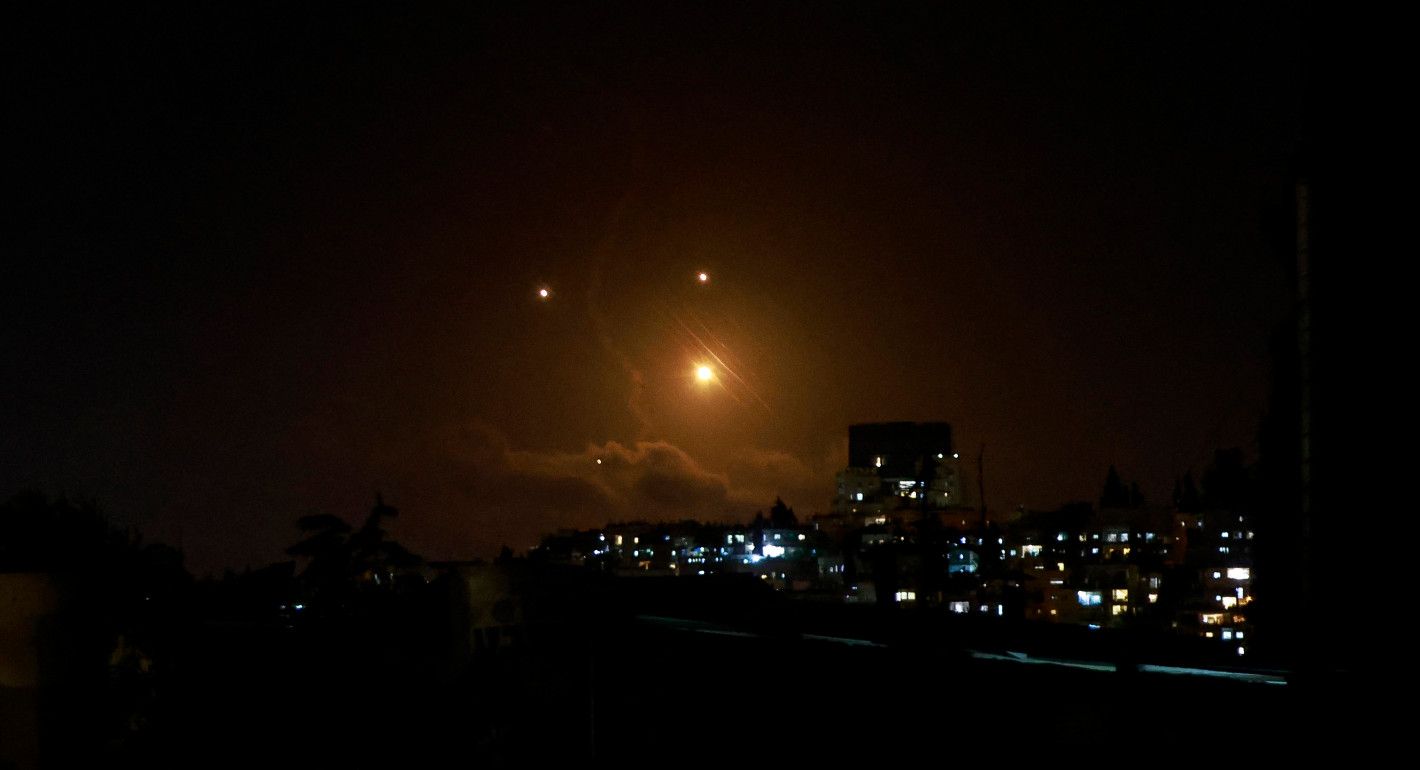 Night sky and buildings illuminated by projectiles in the sky