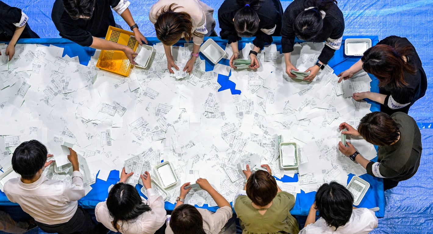 overhead shot of a table with ballots on them and people around the table sorting through them