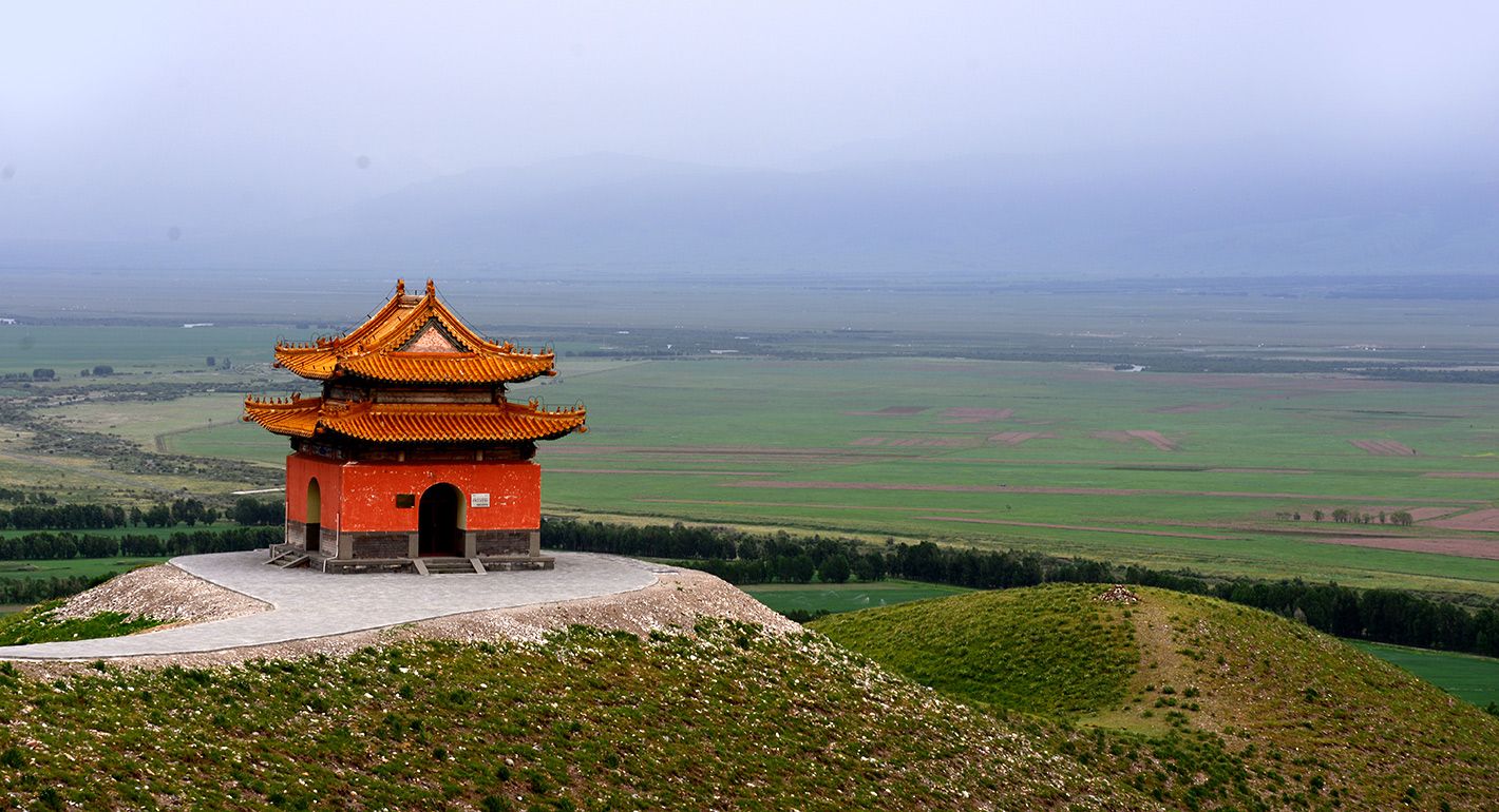 A red monument sits on a hill with green fields in the background.