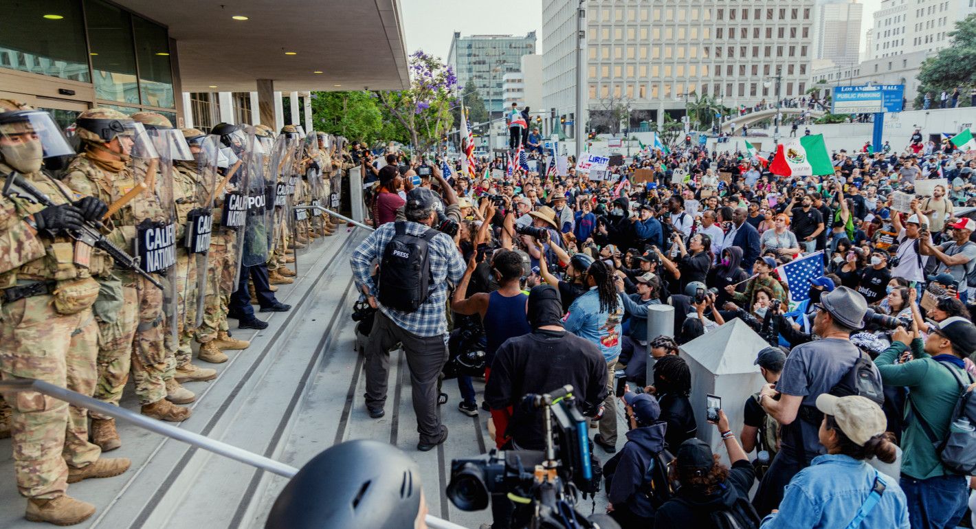 National Guard standing in a line at the top of a building's entrance stairs, with protesters gathered below