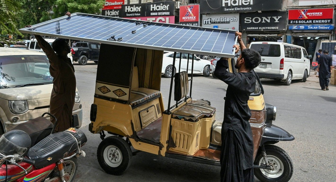Two people putting a solar panel on a rickshaw roof