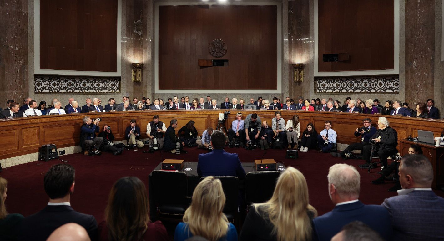 wide room with senators facing an interviewee, with his back to the camera