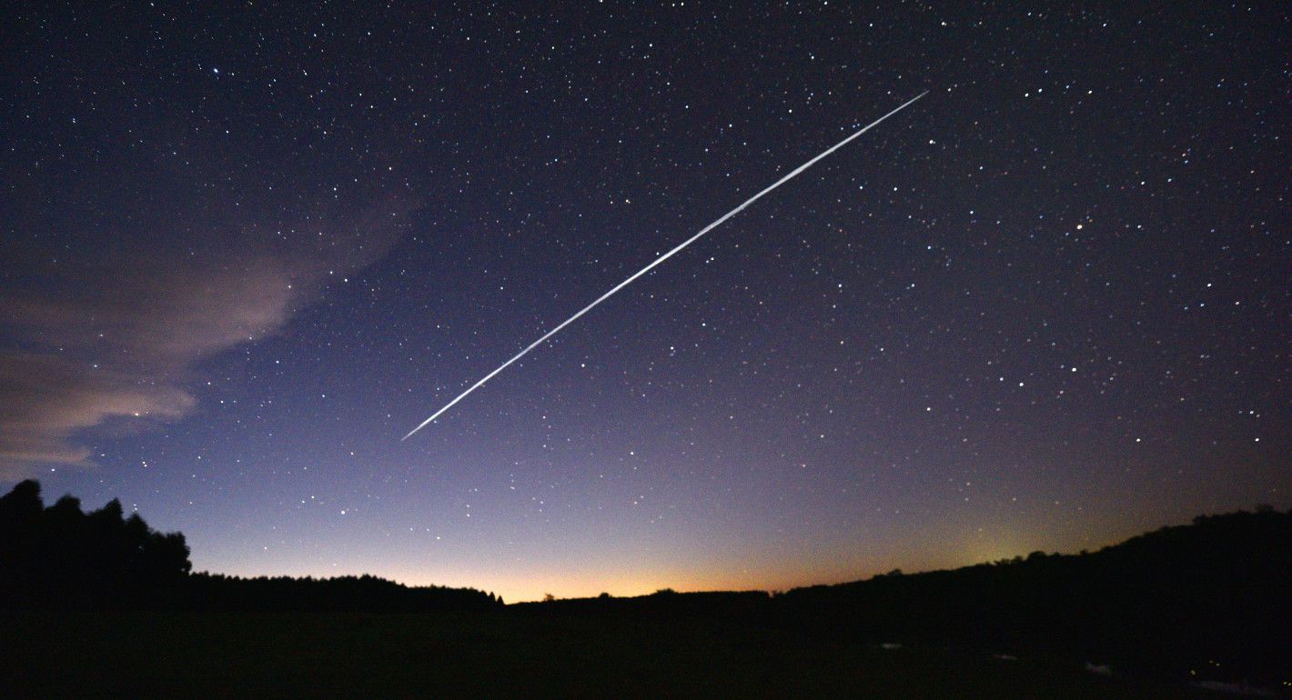 long-exposure night sky image of a white line of Starlink satellites