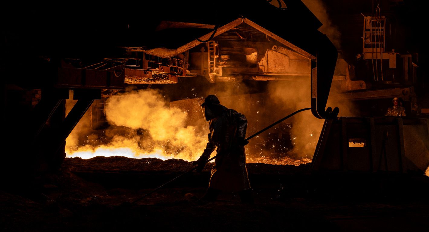 A man in protective gear silhouetted by light from a hot furnace 