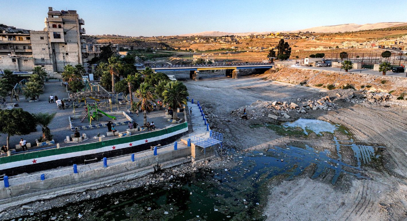 Photo of people walking beside a nearly dry riverbed in Syria.