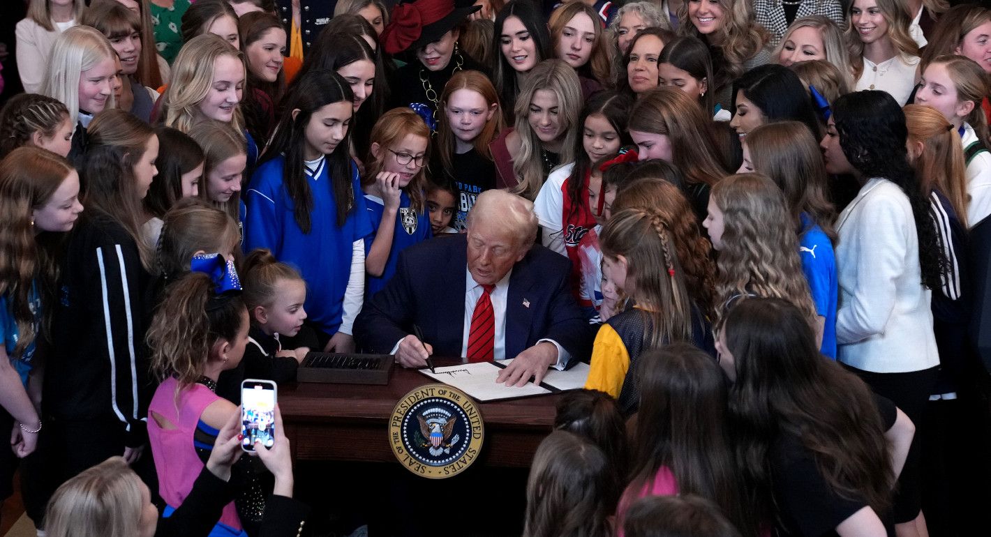 Trump signing a document while surrounded by girls and women