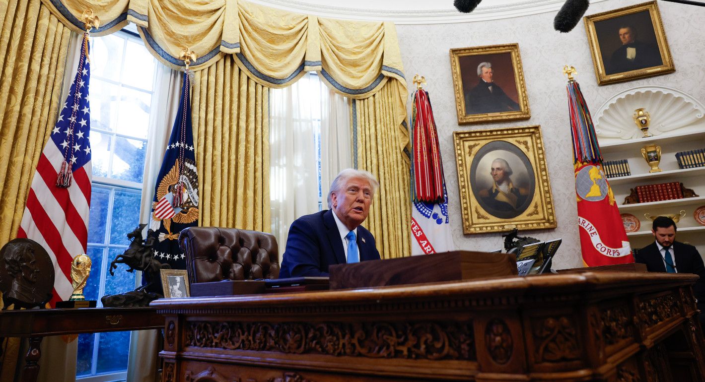 Trump sitting behind a desk talking to reporters