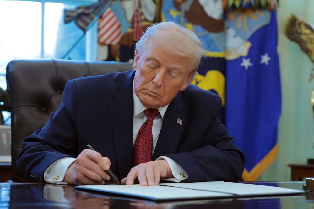Trump sitting at a desk signing a paper