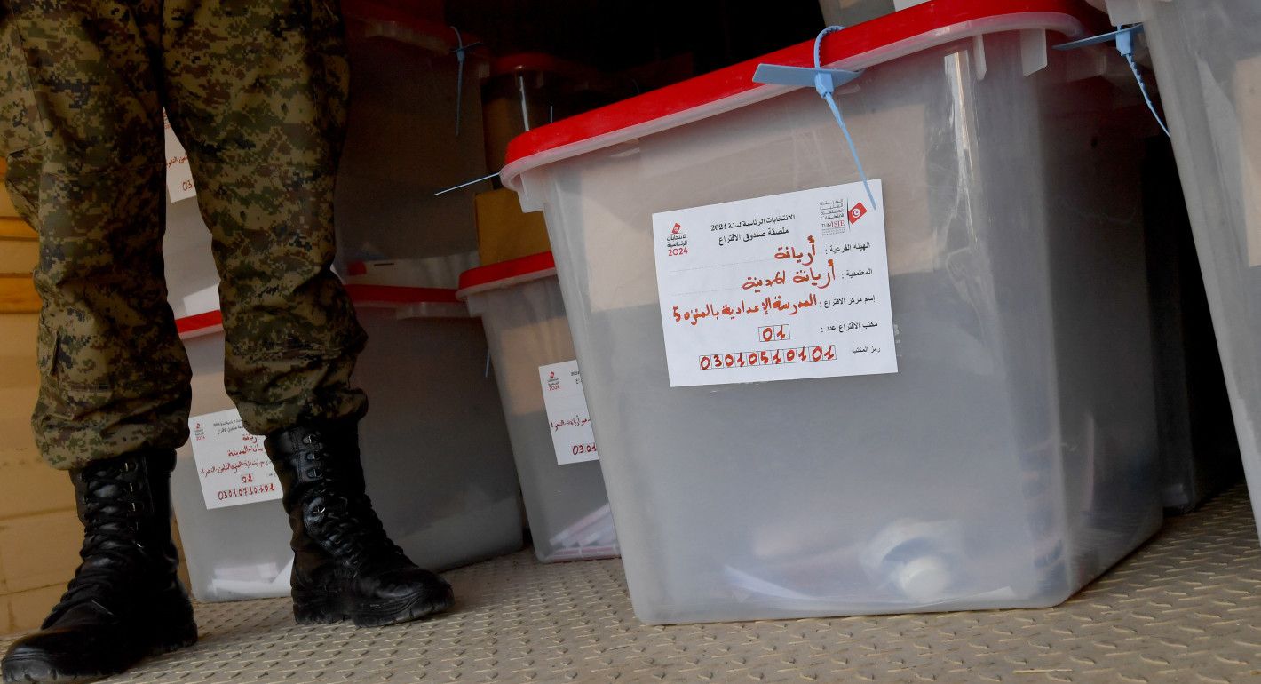 a soldier's boots next to a rubber container used as a ballot deposit box