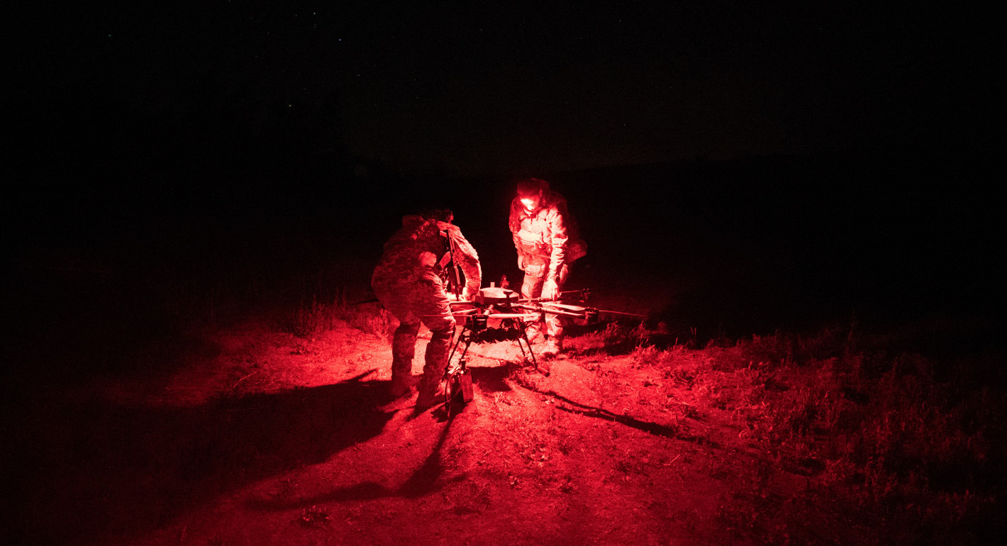 two men crouching over a drone at night, only visible via red light