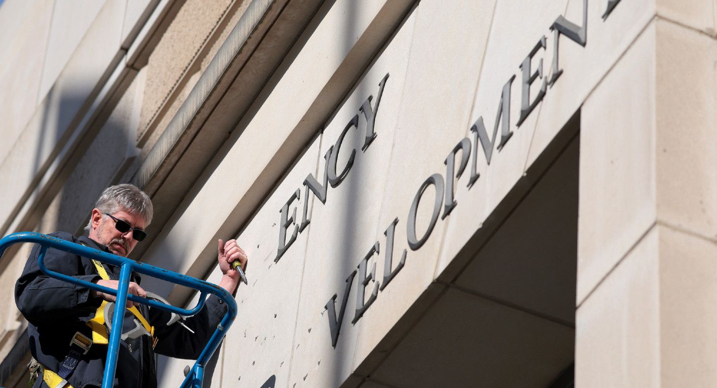 Photograph of a person removing letters from a sign that formerly read "U.S. Agency for International Development."