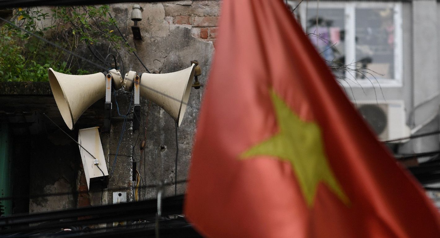 Photo of a set of outdoor loudspeakers hanging on a wall with a Vietnamese flag partially visible in the foreground.