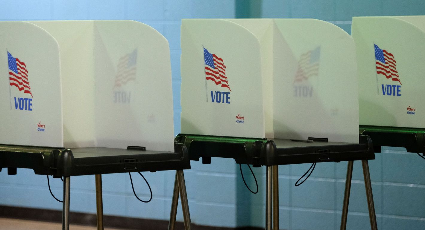 A row of voting booths stands empty in front of a blue wall.